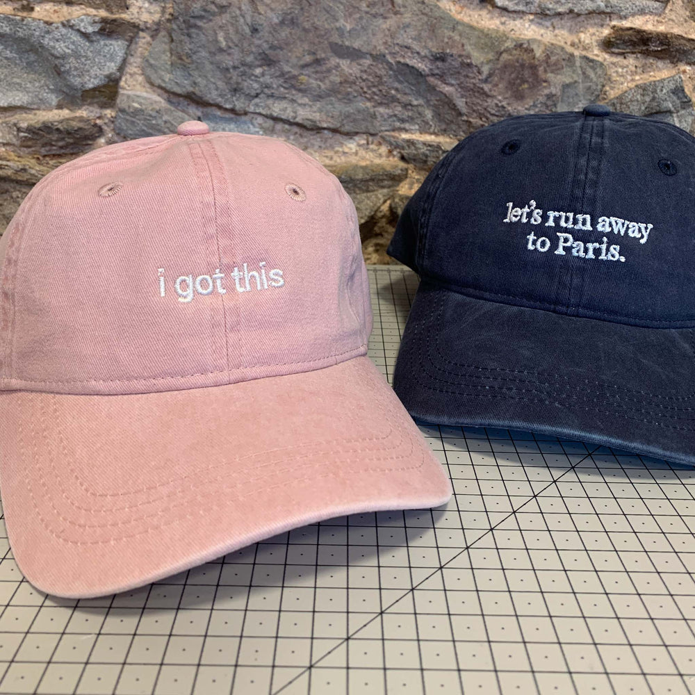 an image showing two organic cotton caps, in blush pink and navy, and with white text embroidered on the front.